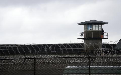 A prison guard stands watch in a tower above barbed-wire fencing. 